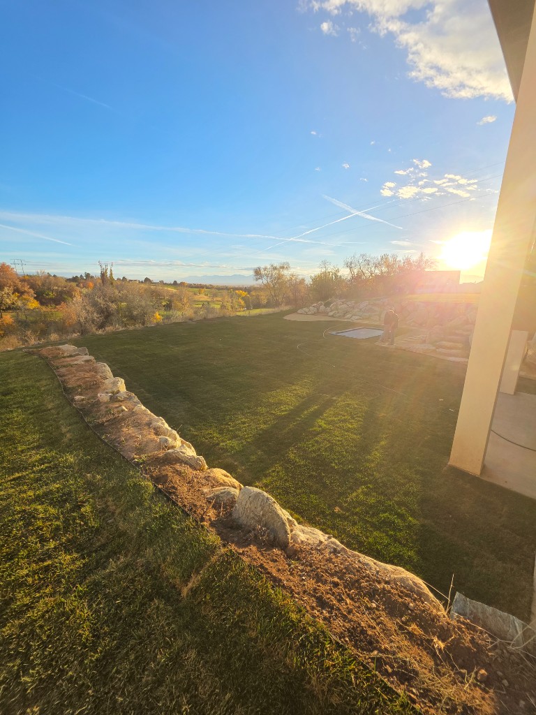 Boulder retaining wall with sod at sunset — Sol Scapes Utah